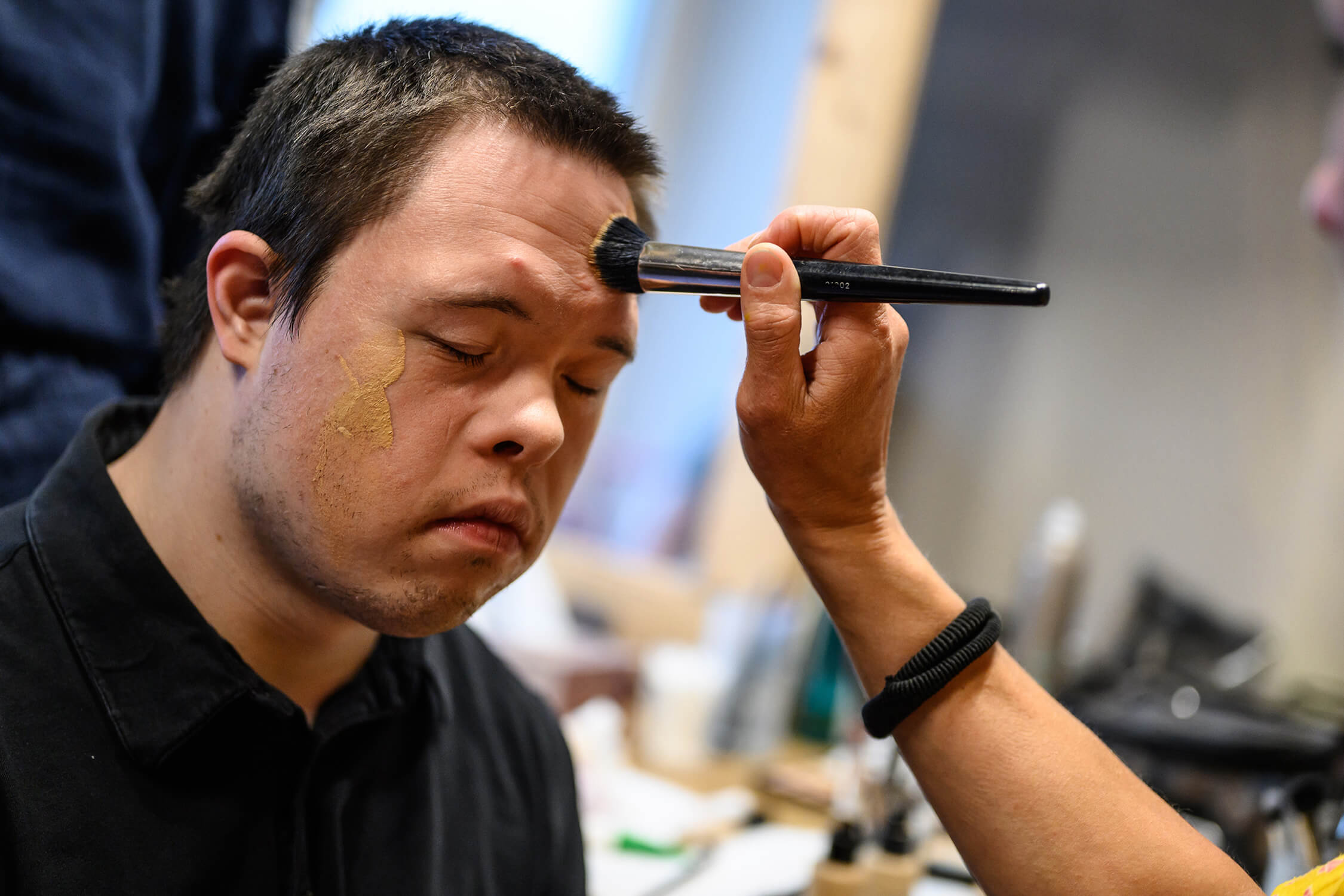 Der Artist Jannic Golm wird vor der Aufführung in der Maske geschminkt.