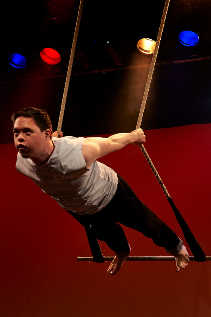 Jannic Golm lehnt sich bei einer Zirkusgala auf dem Trapez kraftvoll nach vorn.
