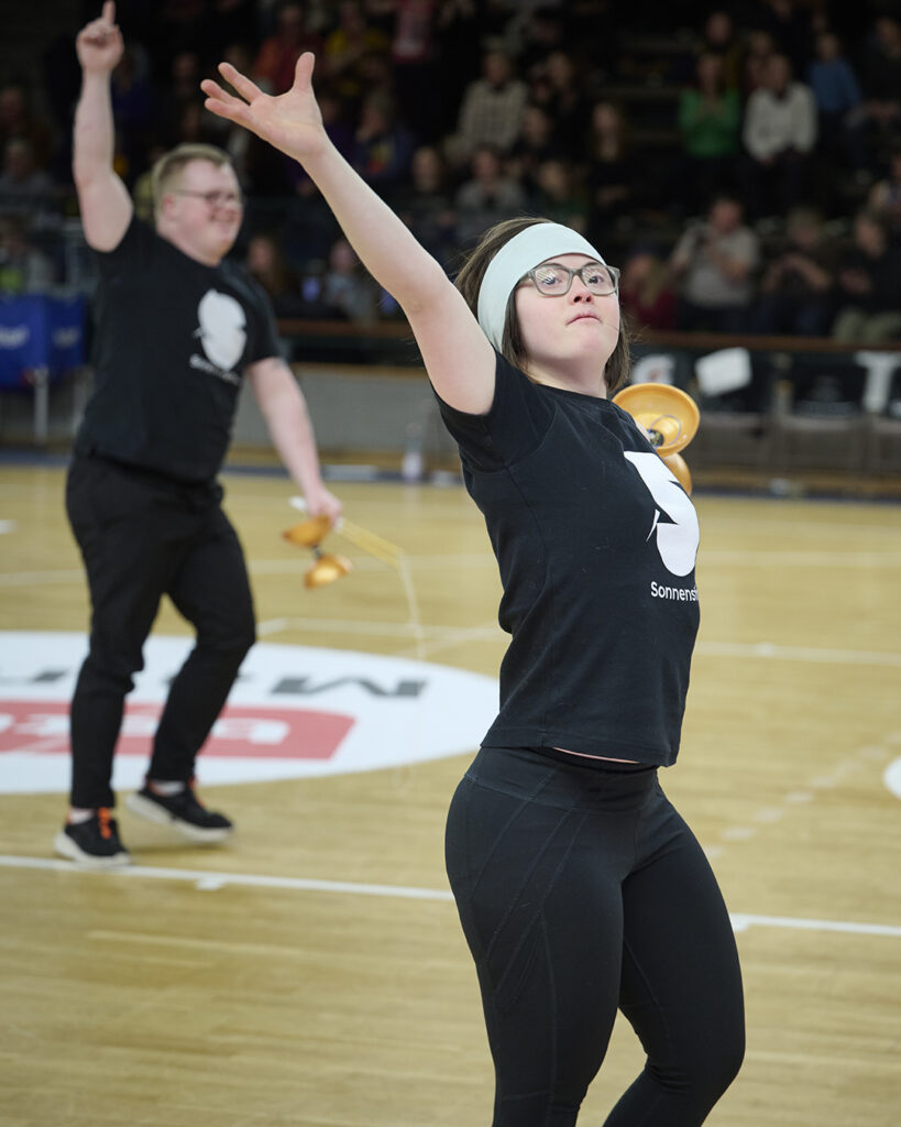 Sonnenstich-Artistin Sol-Rein Saunders präsentiert sich in der Halbzeit-Show bei Alba Berlin dem Publikum. Im Hintergrund sieht man Oskar Schenck.