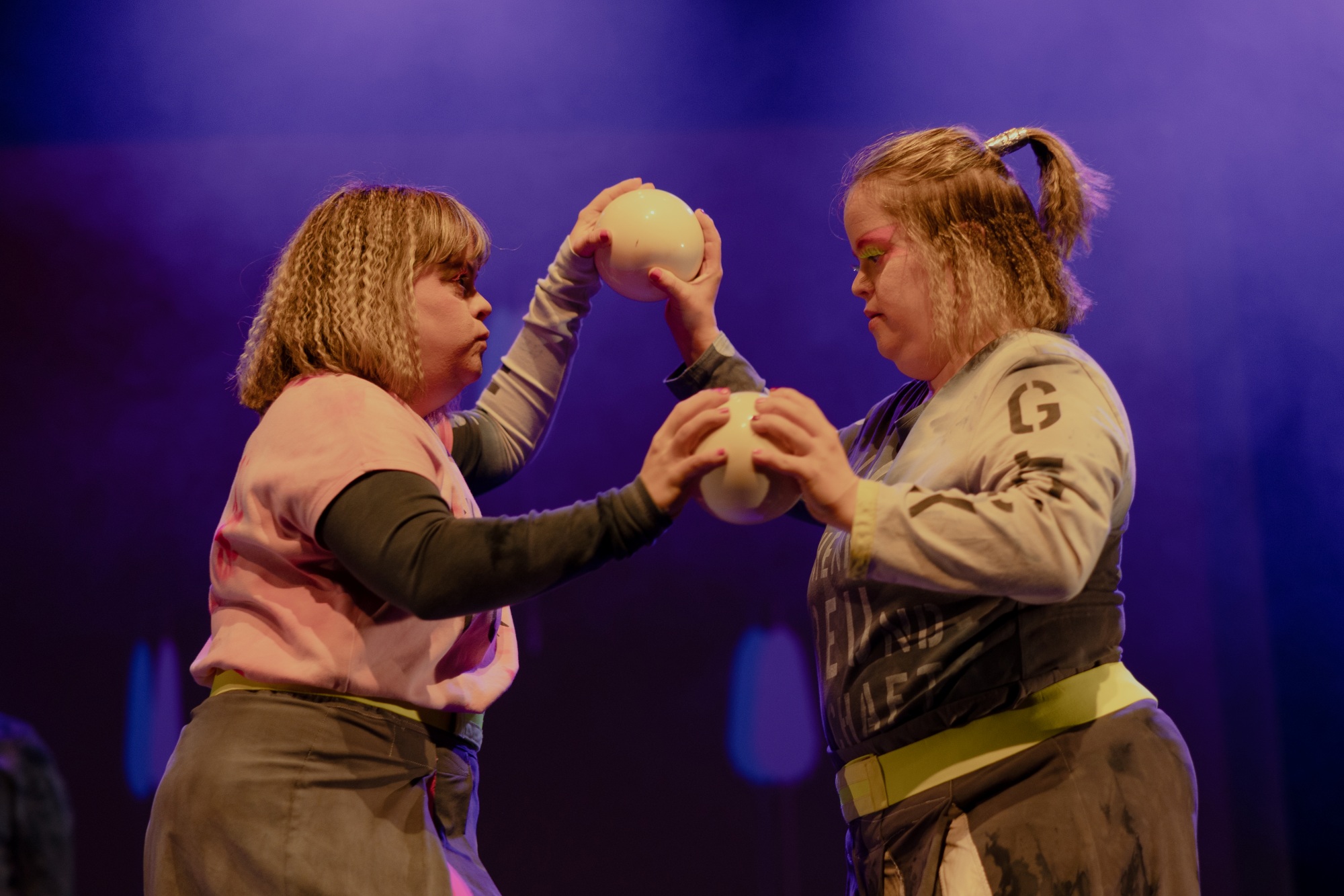 Die Zwillinge Frederike und Ragna Ronacher sind bei einer Balance-Nummer von der Hüfte aufwärts im Profil zu sehen. Ihre Hände sind durch zwei handgroße weiße Kugeln verbunden.