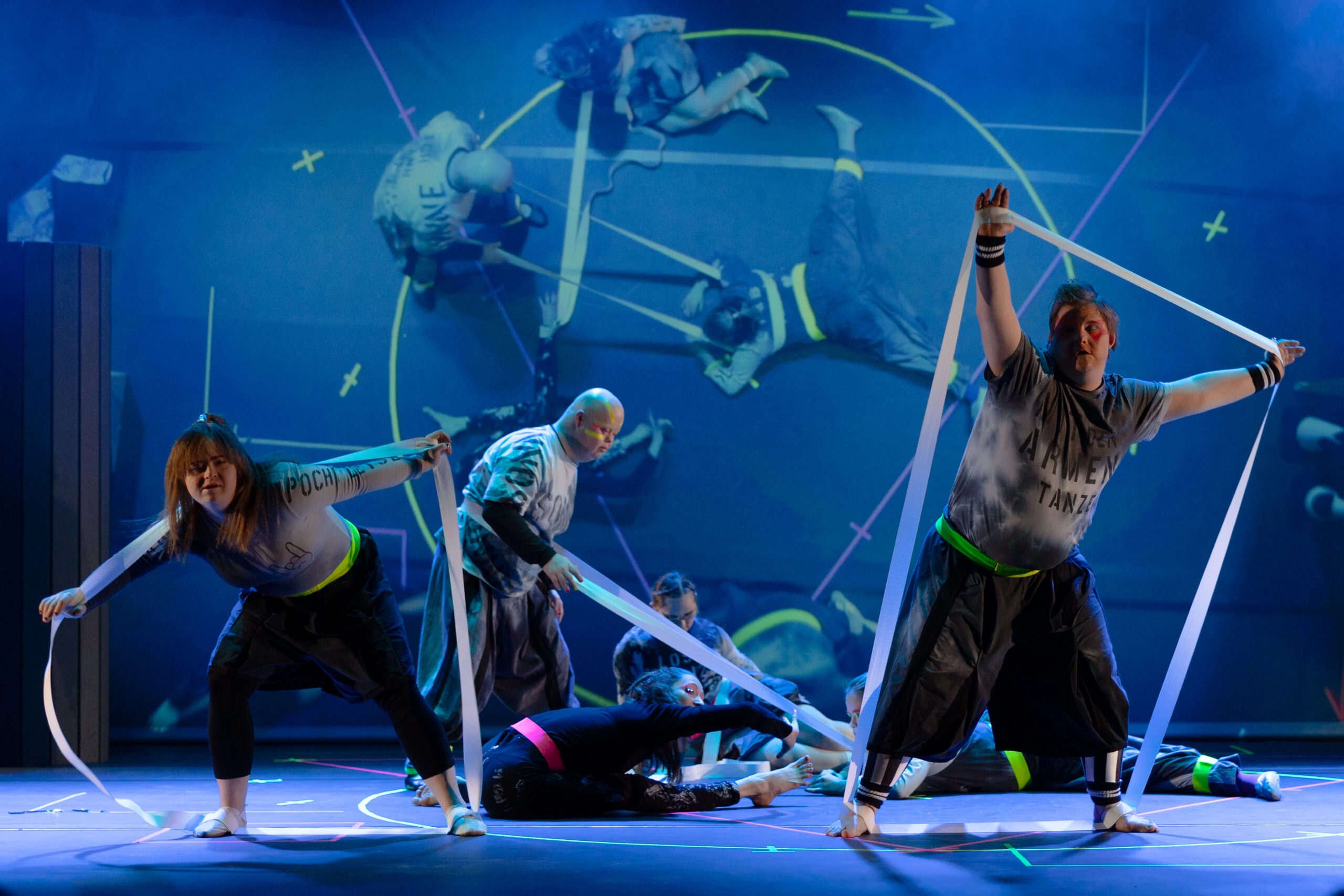 Bei diesem in blau getauchtem Bühnenbild zeigen sechs Artistinnen und Artisten einen Bändertanz. Gleichtzeitig wird per Live-Cam der Tanz auf einen großen Screen im Hintergrund projiziert.